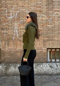 Pulover tricotat cu model în dungi, de culoare verde măsliniu, cu guler din blană, asortat cu pantaloni evazați negri. Ține o geantă mică, neagră, structuratӑ.