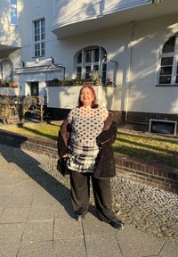 Tenue superposée comprenant un haut transparent à pois, une jupe à volants à carreaux, un pantalon noir à jambes larges et des chaussures plateformes noires épaisses. Sac à main noir inclus.