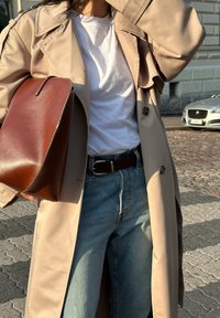 Μπεζ παλτό με λείο υφασμά, που διαθέτει διπλό κούμπωμα και μεγάλα κουμπιά. Μια καφέ δερμάτινη τσάντα συμπληρώνει το μπλε τζιν.