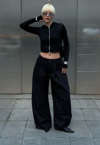 Czarna krótka bluza zapinana na zamek, oversize'owe czarne spodnie z kieszeniami, srebrne akcesoria i okulary przeciwsłoneczne. Gładki materiał, luźny krój, minimalistyczny design.