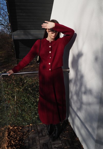 Cárdigan de punto burdeos con detalle de botones, combinado con una falda larga acanalada a juego. Textura suave y diseño ajustado que realza la silueta.