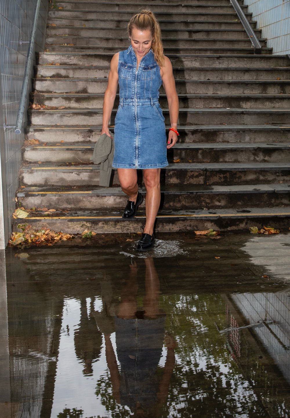 Abito senza maniche in denim, aderente con colletto e cintura in vita; tessuto blu, persona che cammina attraverso acqua bassa con riflessi visibili.