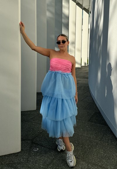 Vestido sin tirantes con un corpiño rosa y falda de tul azul en capas; combinado con zapatillas blancas. Tejido suave y textura blanda.