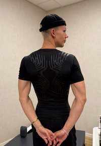 Camisa de atletismo ajustada preta com mangas curtas, apresentando um design texturizado de linhas elevadas nas costas, vestida por uma pessoa de costas.