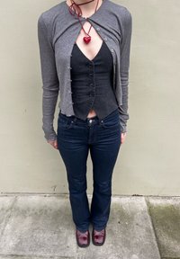 Cardigan cropped cinza de manga longa sobre um colete preto com botões, combinado com jeans flare de denim escuro e sapatos de plataforma vermelhos e brilhantes.