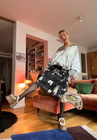 Veste argentée surdimensionnée, jupe noire à motifs, bas résille, chaussures à plateforme duveteuses et un sac unique avec un motif animalier.