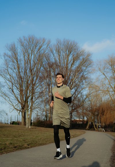 Hombre atlético corriendo por un sendero, vestido con una camiseta de manga corta verde claro y mallas negras, con zapatillas de correr negras y calcetines blancos.