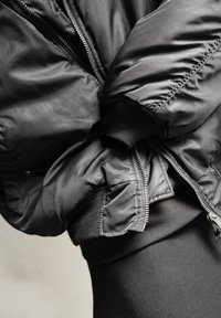 Black bomber jacket with a sleek, shiny exterior, ribbed cuffs, and side pockets. Zippered closure and padded design for warmth.