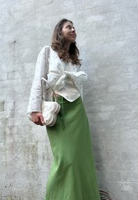 Haut à manches longues blanc avec motifs floraux texturés, noué à l'avant ; jupe maxi fluide verte ; sac à main crème avec des accents arrondis.