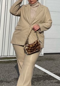 Μπεζ τεχνητό δερμάτινο κοστούμι με μονό κουμπί, δύο μπροστινές τσέπες και ταιριαστά παντελόνια ψηλής μέσης. Στολισμένο με τσάντα με υφή φουρκέτας και αλυσίδα.