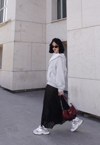 Grey oversized hoodie, white top, black lace skirt, silver trainers, and a small red handbag. Standing on a paved surface next to a building.