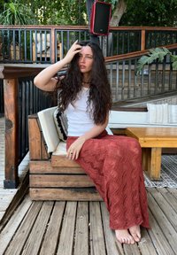 Maxi suknja u boji hrđe s teksturom čipke u zig-zag uzorku, uparen s bijelim uskim topom, sjedi na drvenoj klupi u dvorištu.