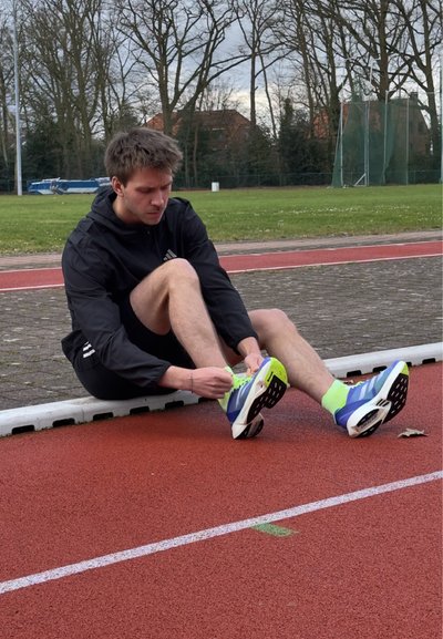 Zapatillas deportivas con una combinación de colores azul, blanco y verde brillante; diseño ligero. Atando individualmente cordones verdes brillantes en la pista de atletismo.