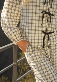 Kostým pyžama v bielej a čiernej farbe so skontrolovaným vzorom, voľný strih, šnúrkové detaily a vrecká v topce a nohaviciach. Mäkká textúra látky.