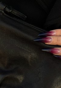 Zwarte leren tas met een gestructureerd oppervlak en een subtiel logo. De vingernagels zijn lang en verlopen van paars naar donkerblauw.
