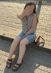 Brune lær sandaler med dobbel spænde, grå ærmeløs bluse og denim shorts. Lille brun crossover taske på en betonoverflade.
