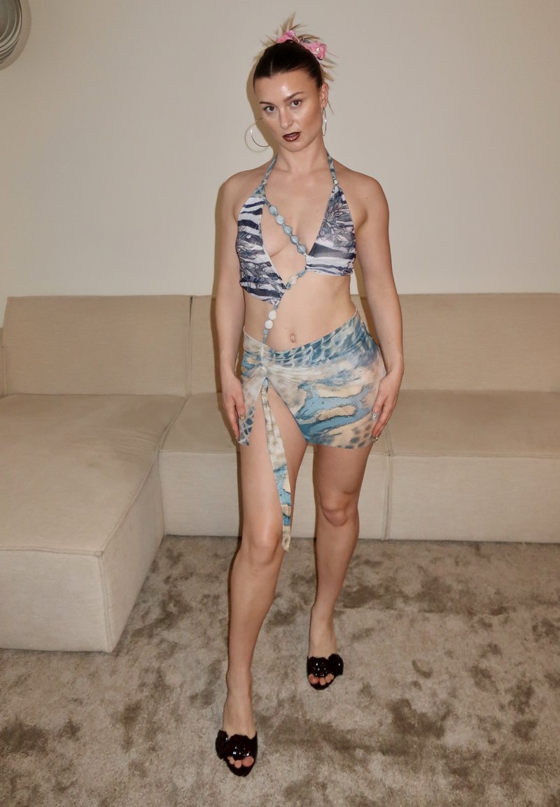 Haut de bikini style dos nu avec un motif abstrait bleu et blanc, associé à une mini-jupe portefeuille assortie. Orné d'accents circulaires.