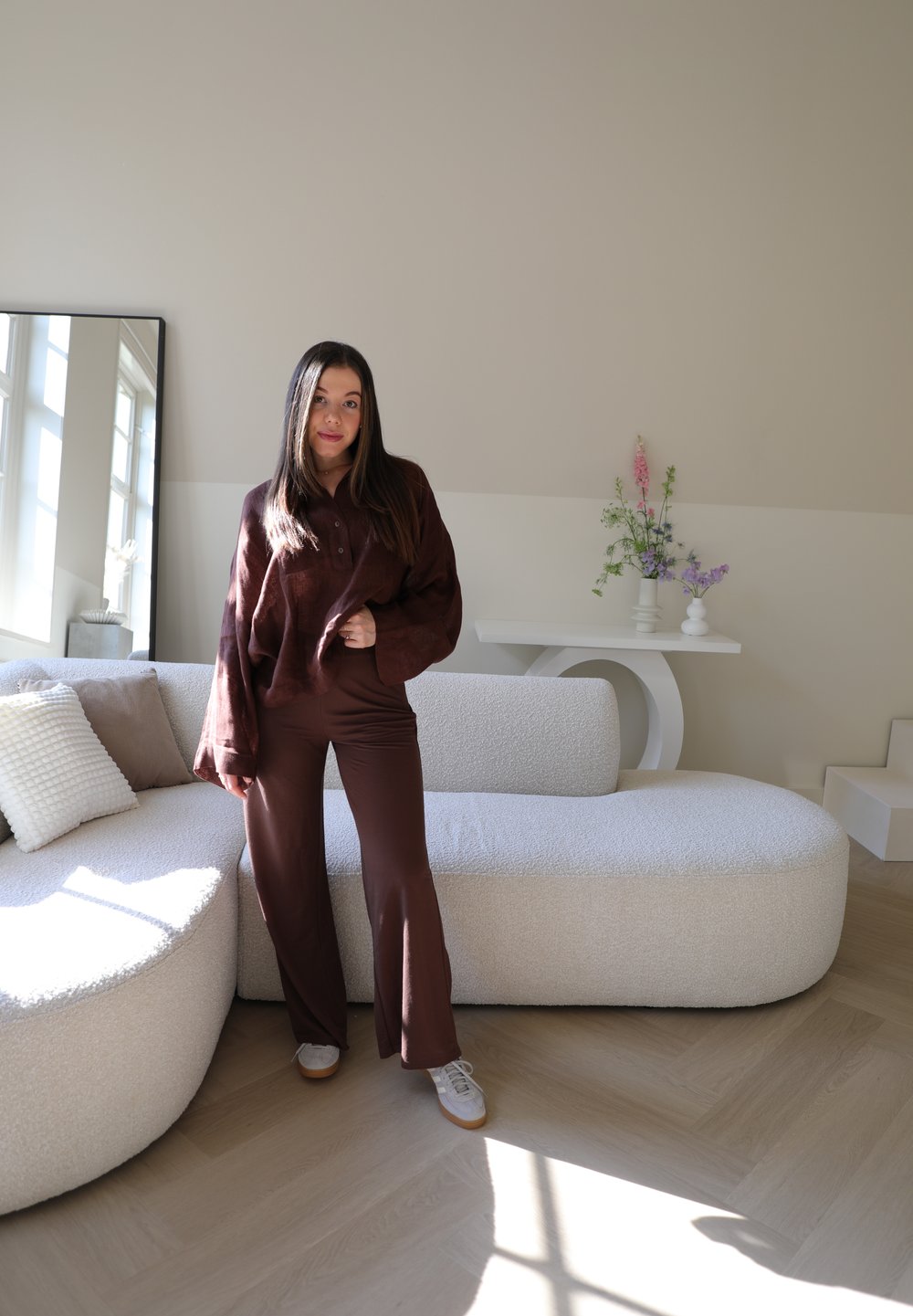 Καφέ, υφασμάτινο, υπερμεγέθες πουκάμισο και ταιριαστά καμπάνα παντελόνια. Λευκό, υφασμάτινο καναπέ με δύο ουδέριες μαξιλάρες. Ήπιος φωτισμός ενισχύει τη σκηνή.