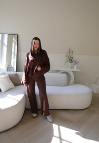 Καφέ, υφασμάτινο, υπερμεγέθες πουκάμισο και ταιριαστά καμπάνα παντελόνια. Λευκό, υφασμάτινο καναπέ με δύο ουδέριες μαξιλάρες. Ήπιος φωτισμός ενισχύει τη σκηνή.