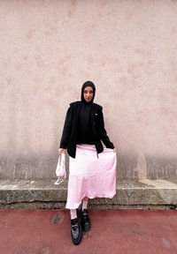 Μαύρο γιλέκο φλις πάνω από μαύρη μπλούζα, συνδυασμένο με μια ανοιχτό ροζ φούστα. Μαύρες ψηλές πλατφόρμες και μια μικρή ροζ τσάντα ολ οκληρώνουν το ντύσιμο.