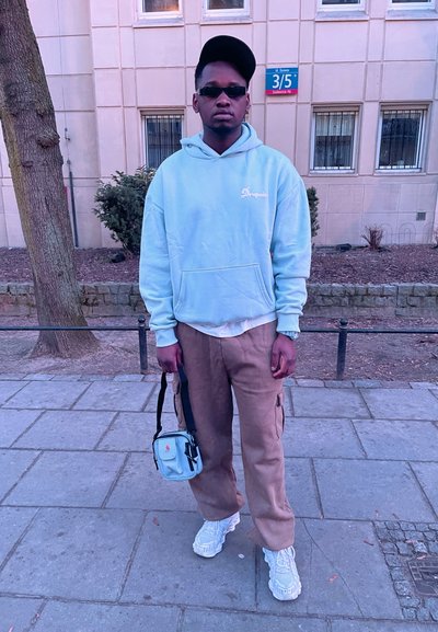 Sudadera azul claro, pantalones cargo beige, zapatillas blancas, bolso cruzado azul pequeño. Los accesorios incluyen gafas de sol y una gorra negra.