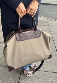 Mala de nylon bege com detalhes em pele estampada de croco castanha, duas alças superiores e uma alça de ombro destacável. Fecho com zíper no topo.