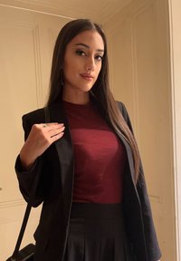 Μαύρο σακάκι πάνω από μπορντό τοπ, συνοδευόμενο από μαύρη ψηλόμεση φούστα. Λείες υφές, ελάχιστα μεταλλικά στοιχεία και διακριτικά αξεσουάρ.