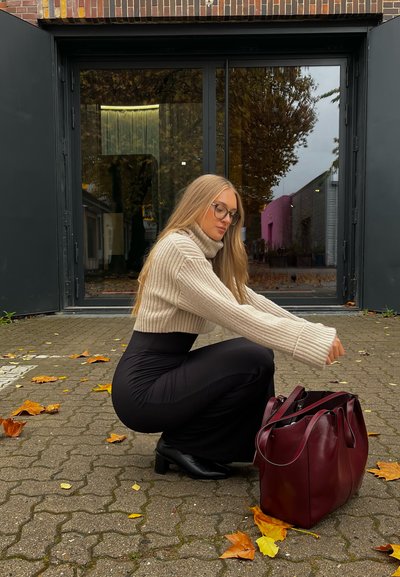 Bolso de cuero burdeos con textura suave y asas dobles, combinado con un suéter de cuello alto de canalé en crema y una falda negra ajustada.