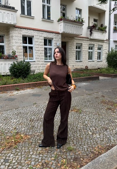 Top de punto sin mangas en marrón combinado con pantalones anchos de textura marrón oscuro. Accesorios incluyen un bolso negro y una pulsera marrón.