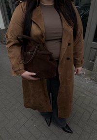 Trench coat de camurça castanho, blusa ajustada bege, bolsa de camurça castanha, jeans escuros, sapatos de salto agudo pretos; textura suave e design clássico.