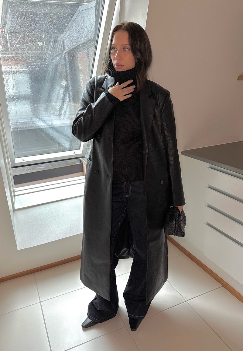 Fekete bőr, dupla soros kabát fekete garbóval, sötét farmernadrággal és hegyes orrú fekete csizmával párosítva.