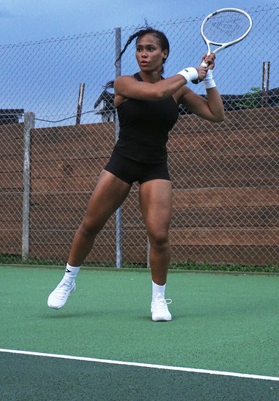 Jugadora de tenis femenina en un uniforme atlético negro, lista con una raqueta blanca en una cancha verde. Entre las características notables se incluye un fondo de cerca de eslabones de cadena.