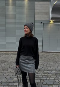 Μαύρη μπλούζα, γκρι σκουφάκι, ασημί φούστα, μαύρες καλσόν, κρατώντας μια γκρι τσάντα. Υφές υλικών και στρωματοποιημένος σχεδιασμός, με άνετη εφαρμογή.