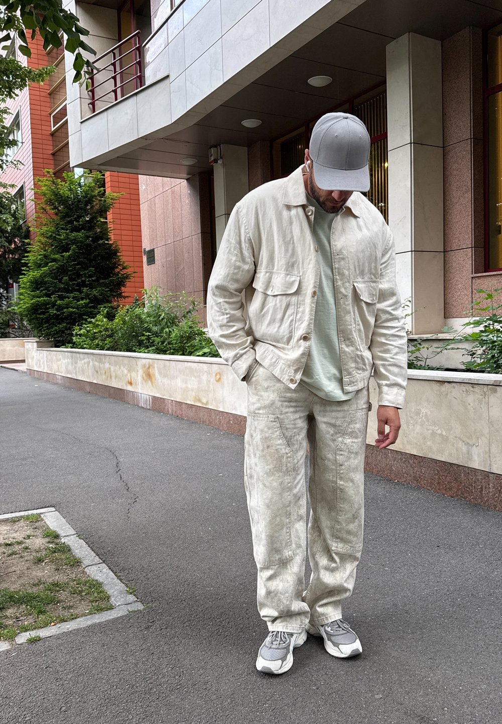 Ljust beige linnejacka med två bröstfickor, matchad med lösa byxor. Under jackan en ljusgrön skjorta och grå sneakers.