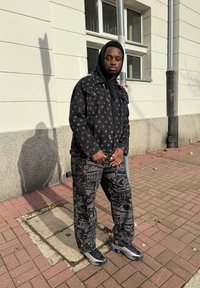 Casaco de ganga preto com logótipos discretos, combinado com calças pretas com padrão. Ambos têm um corte descontraído, complementados por ténis que completam o visual.