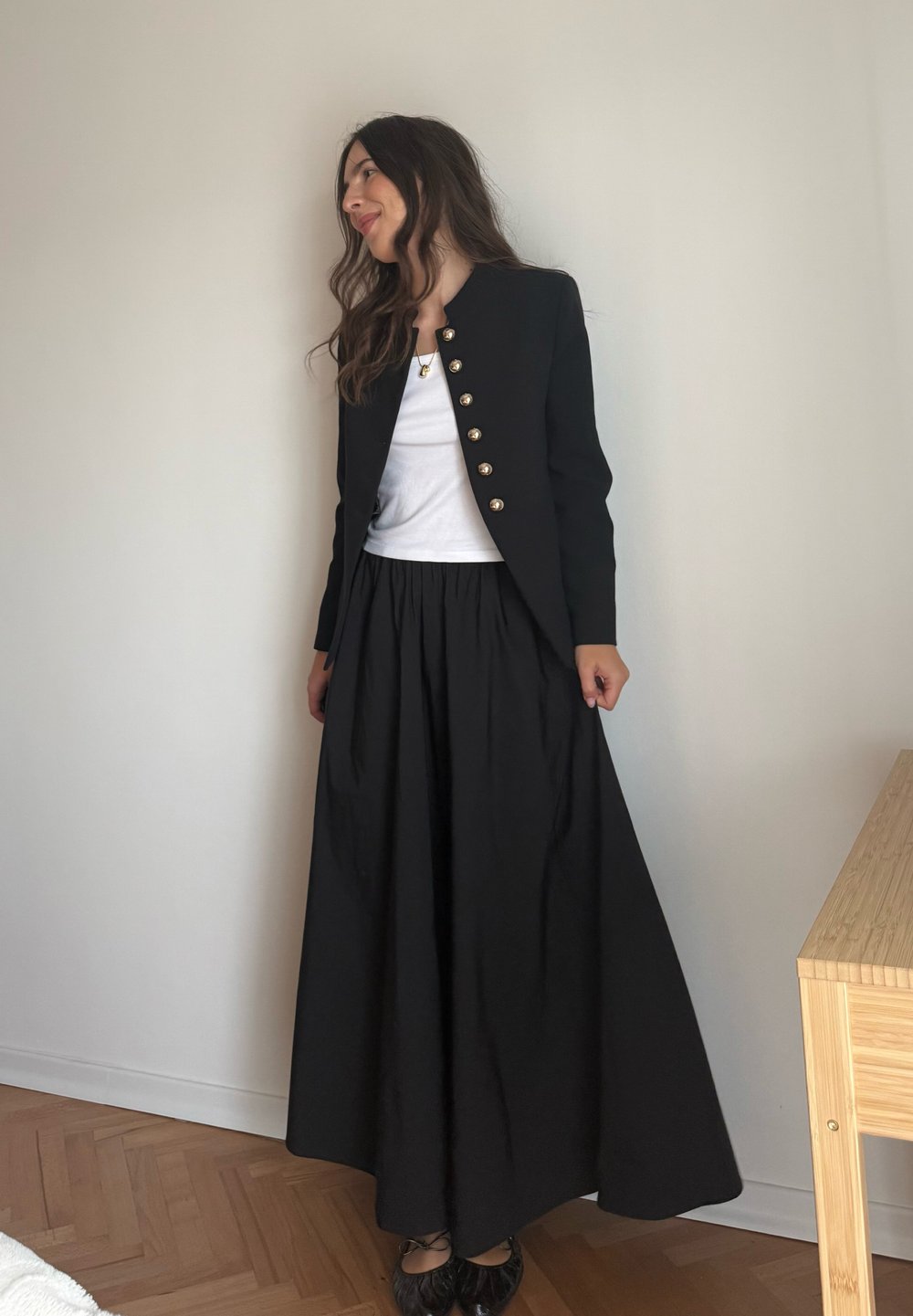 Schwarzer Blazer mit goldenen Knöpfen, weißem Oberteil und schwarzem Maxikleid. Glatte Stoffe, taillierte Passform, ausgestellt Rock und flache Schuhe runden das Outfit ab.