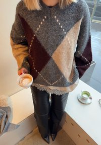 Hall ja beež argyle-mustriga kudumissviiter, millel on marooni aktsendid, kantud valge pitsäärisega topi kohal; kombineeritud mustade nahkkolmustega.