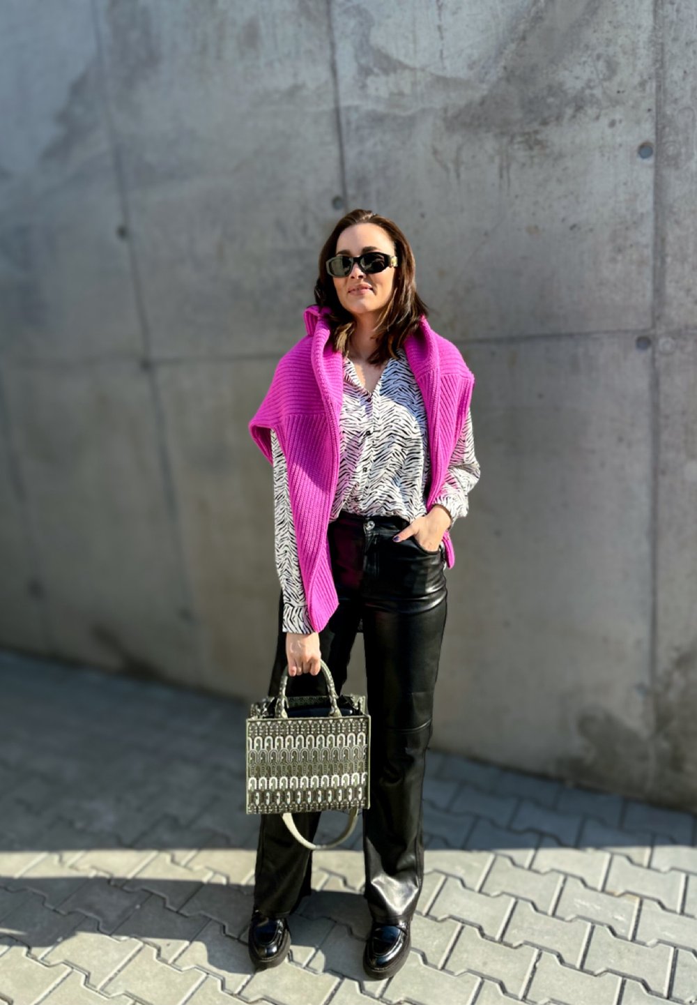 Chaleco de punto rosa sobre una blusa de estampado de cebra en blanco y negro, combinado con pantalones de cuero negros y un bolso estampado. Zapatos negros.