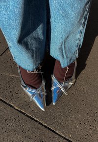 Zilveren puntige hakken met een glanzende lakleren afwerking. Gestyleerd met donkerbruine geribde sokken en gecombineerd met blauwe spijkerbroek.