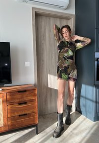 Φόρεμα από διαφανές ύφασμα με καμουφλάζ και μακριά μανίκια, μήκους μέχρι το γόνατο, που συνδυάζεται με μαύρες μπότες μέχρι τον αστράγαλο με ασημένια εξαρτήματα.