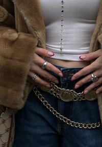 Ψεύτικο γούνα παλτό, λευκή μπλούζα crop top, μπλε τζιν παντελόνι, χρυσή ζώνη με κυκλικές λεπτομέρειες, ασημένια δαχτυλίδια και νύχια με ροζ άκρες.