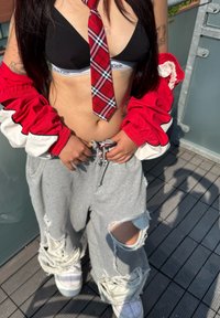 Svart bralette med vit band, röd rutigt slips, röd och vit jacka, grå slitna sweatpants och vita plattformssneakers.