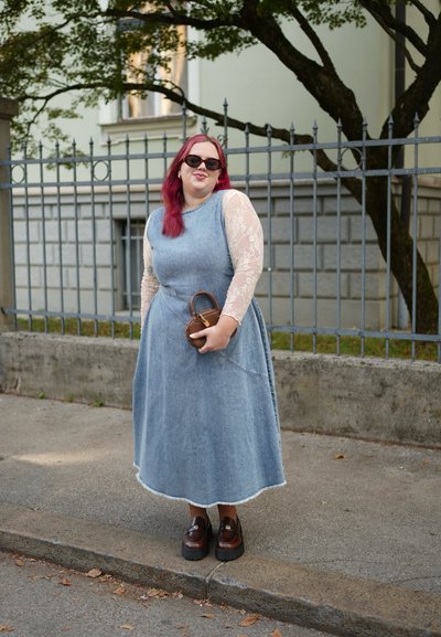 Vestido maxi de mezclilla con mangas largas de encaje, con bolsillos laterales y un dobladillo deshilachado. Mocasines marrones y un bolso pequeño completan el look.