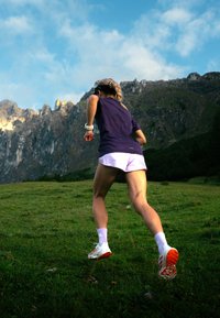 Lilla fukttransporterende skjorte, hvite shorts og rødtrimmede joggesko. Figuren løper på gress med fjell i bakgrunnen.