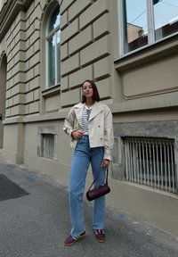 Jachetă cropped bej deschis, cămașă cu dungi, blugi drepti albaștri și geantă adânc purpurie cu un model texturat. Tenisi cu accente întunecate.