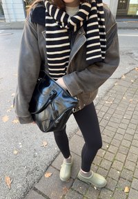 Brun skinnjacka, svartvitrandig halsduk, svart lackväska, svarta leggings, gröna slip-on skor, texturerad trottoar.