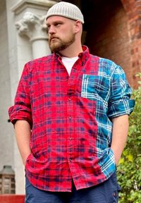 Camisa de flanela às riscas vermelhas e azuis, com botão à frente, mangas arregaçadas e um bolso contrastante com padrão xadrez.