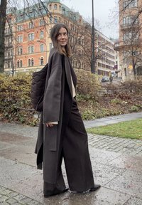 Oversizowy ciemnoszary płaszcz noszony na czarnym dzianinowym topie i szerokich spodniach. Dodatki to pikowany czarny plecak i ciemne botki za kostkę. Miejski klimat.