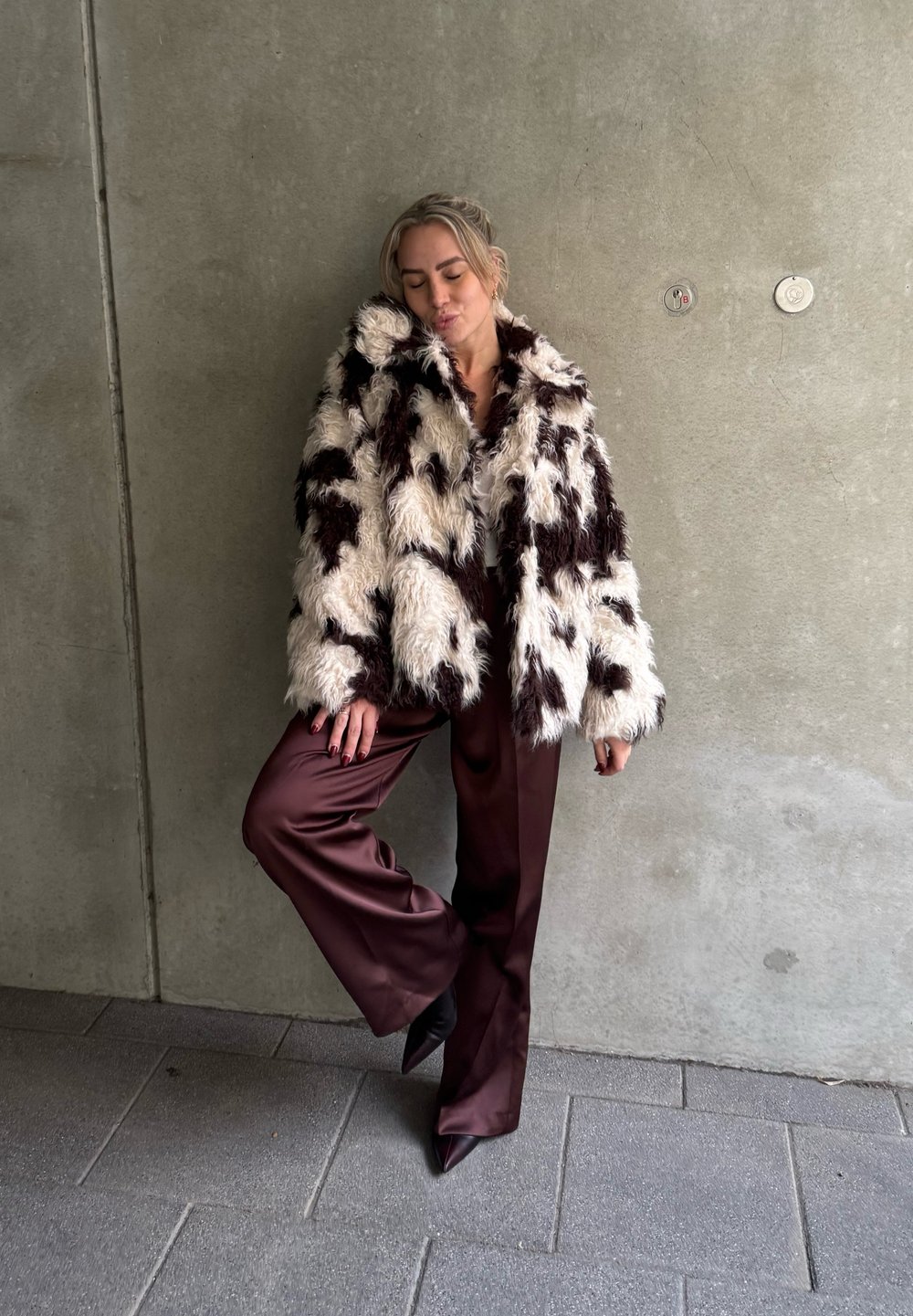 Fuskepelsjakke med en blanding av hvite og brune felter, brede slag, kombinert med burgunderrøde satengbukser. Teksturert, voluminøst design.