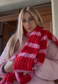 Punavalkoiset raidalliset neulotut huivit pidetään edessä, teksturoidulla, paksulla designilla. Yhdistetty vaaleanpunaiseen toppatakkiin.